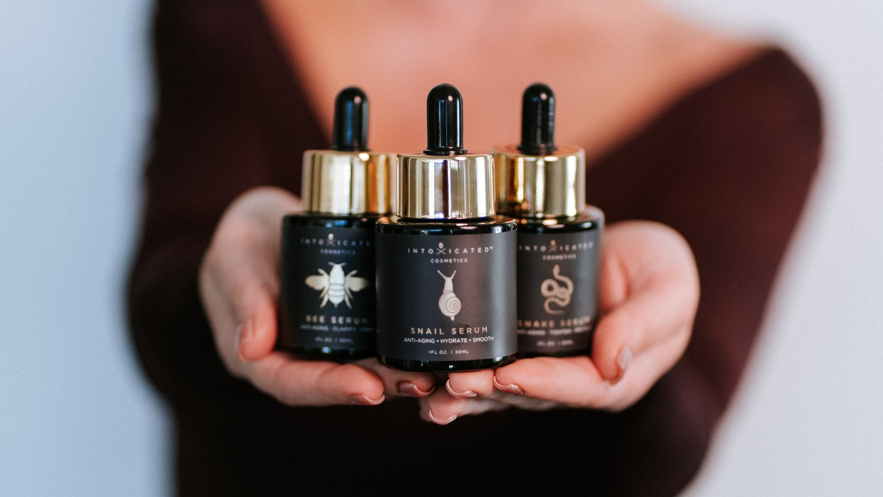 Three black and gold skincare bottles held in a hand against a neutral background